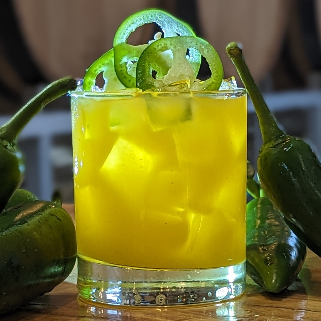 Tijuana Go Surfing, yellow cocktail in rocks glass. Made with Jalapeno Vodka and mango juice. garnished with jalapenos